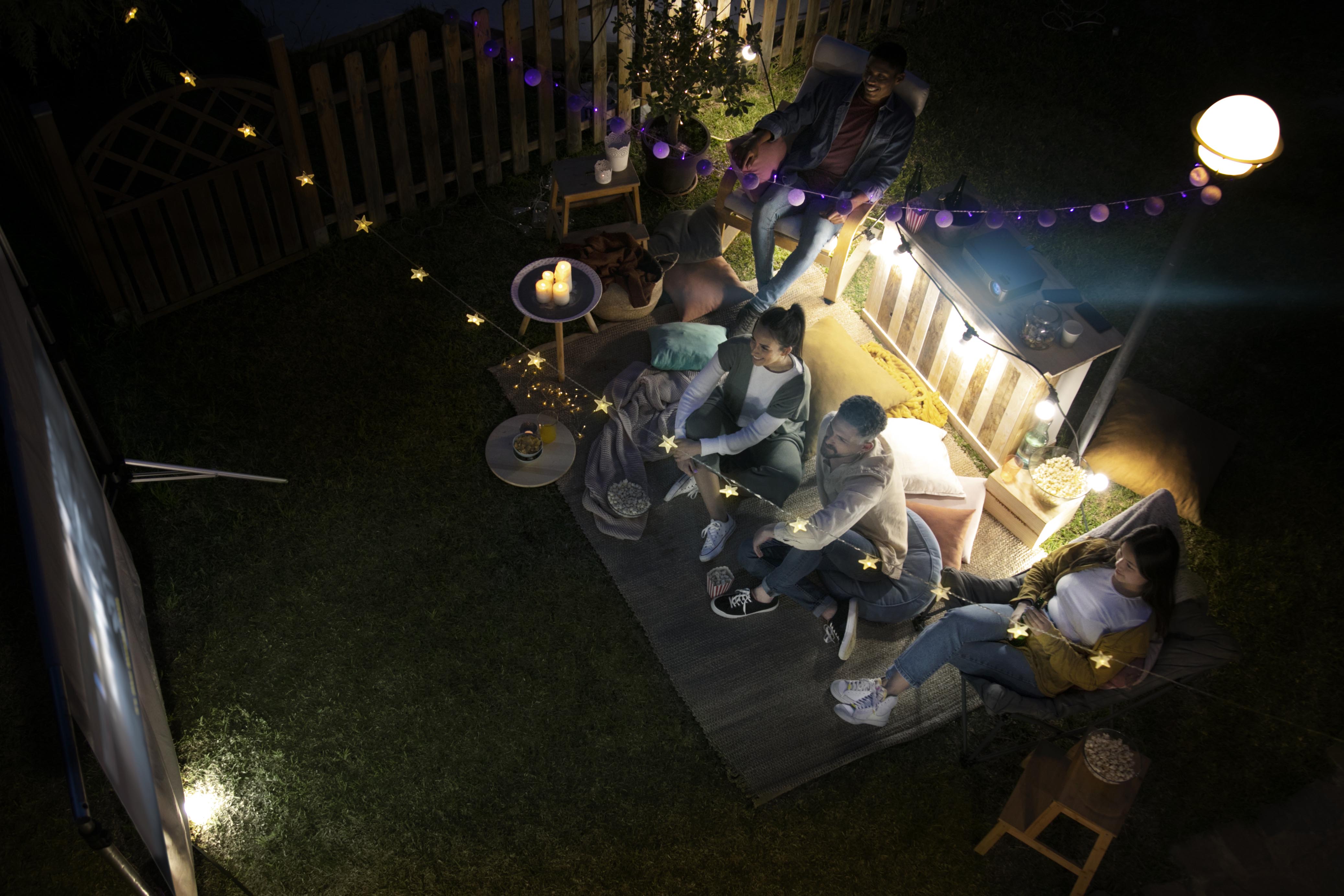 حفلة بسيطة على سطح المنزل بأجواء شبابية، مع إنارة خفيفة، طاولة سناك، وزينة ناعمة تضفي جوًّا دافئًا وعفويًا